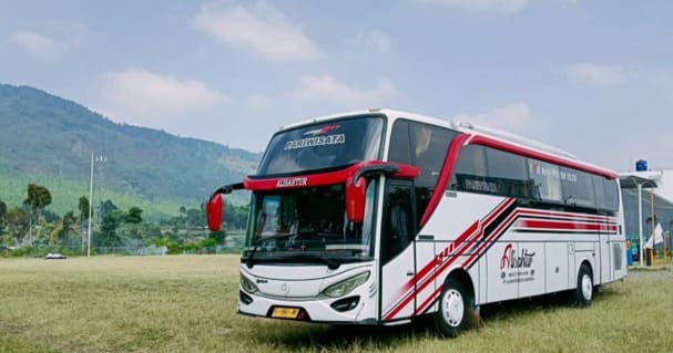 Modern white charter bus on Indonesian highway with mountain background